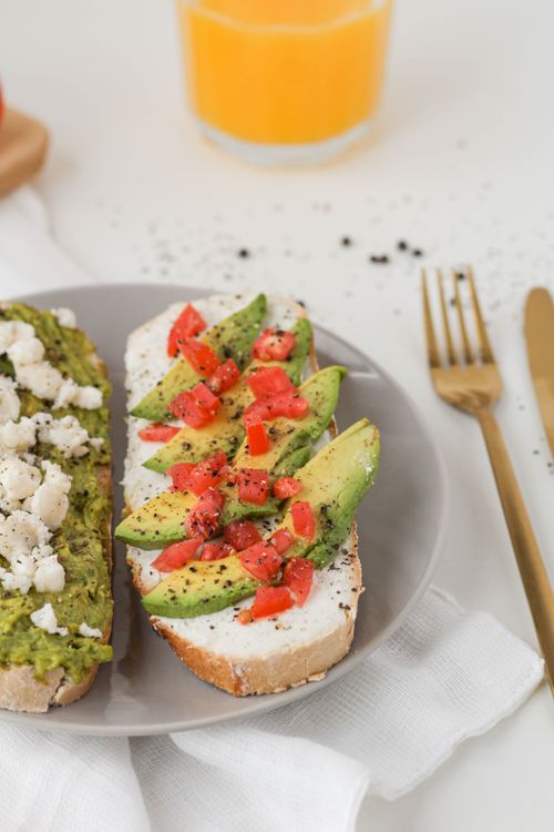 Free Close-up of delicious avocado toast topped with fresh tomatoes, cheese, and pepper on a plate. Stock Photo