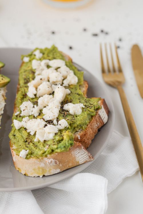 Free Healthy avocado toast with a crumbled cheese topping on a white plate, perfect for breakfast. Stock Photo