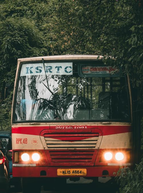 Free A red KSRTC bus navigates a narrow forested road, showcasing public transport in India. Stock Photo