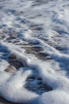A detailed view of seafoam covering the sandy beach, capturing the ocean's gentle waves and textures.