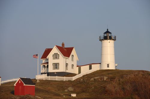 Free A picturesque lighthouse and house standing on a scenic coastal hill against a clear sky. Stock Photo