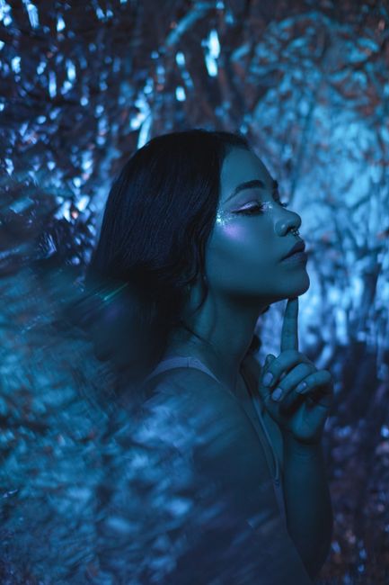 A striking profile of a woman posing against a shimmering blue background with artistic lighting.