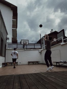 Two men playing basketball in a residential courtyard, shooting hoops.