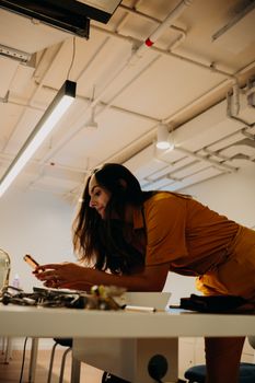 Young woman texting on smartphone, leaning over a desk in a modern office setting.