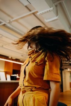 A woman in a vibrant outfit flipping her hair in a modern indoor environment.