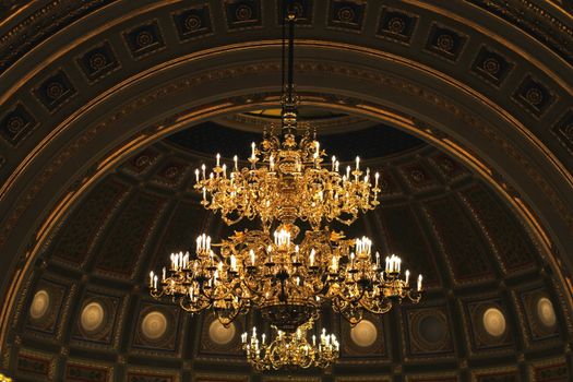 A magnificent chandelier illuminates an opulently designed dome ceiling, exuding elegance and luxury.