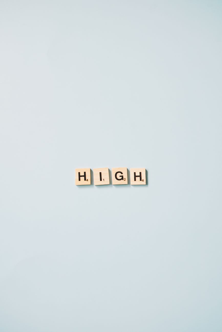 Minimalist art featuring Scrabble tiles spelling 'HIGH' on a light blue background.