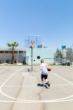 A child dribbling a basketball on an outdoor court under a clear blue sky, showcasing active sports.