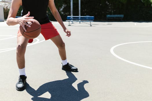 A young adult male dribbles a basketball on an outdoor court under clear daylight.