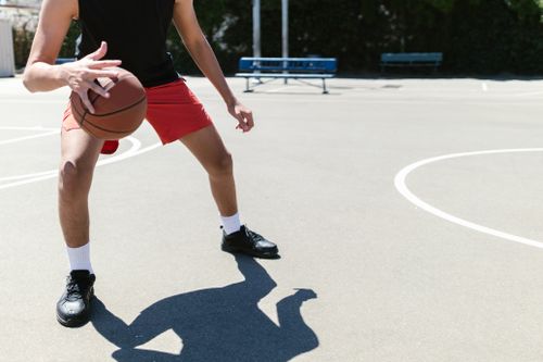 Free A young adult male dribbles a basketball on an outdoor court under clear daylight. Stock Photo