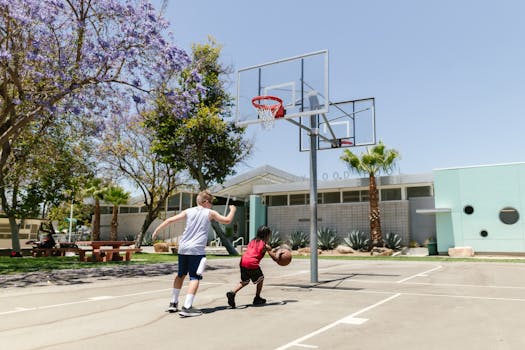 Two boys playing basketball outdoors on a sunny day at school court.