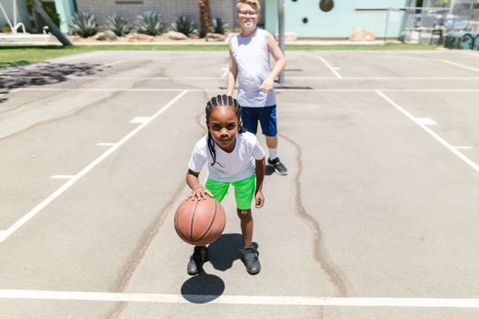 Two children playing basketball on an outdoor court during the day.