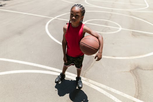 Young boy standing on an outdoor basketball court holding a basketball. Daytime scene.