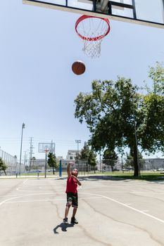 Young boy enjoying a sunny day playing basketball alone on an outdoor court.