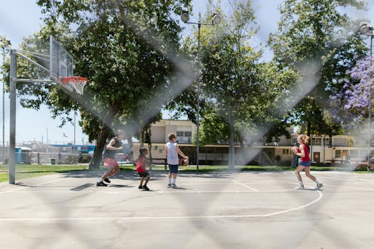 Children playing basketball on an outdoor court in a park setting, showcasing diversity and fun.