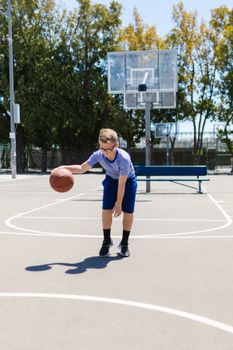 Young boy dribbling basketball outdoors on a sunny day.