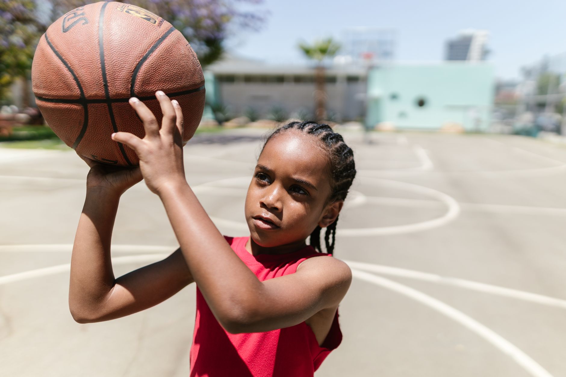 Young child practicing basketball skills on an outdoor court in bright sunlight.