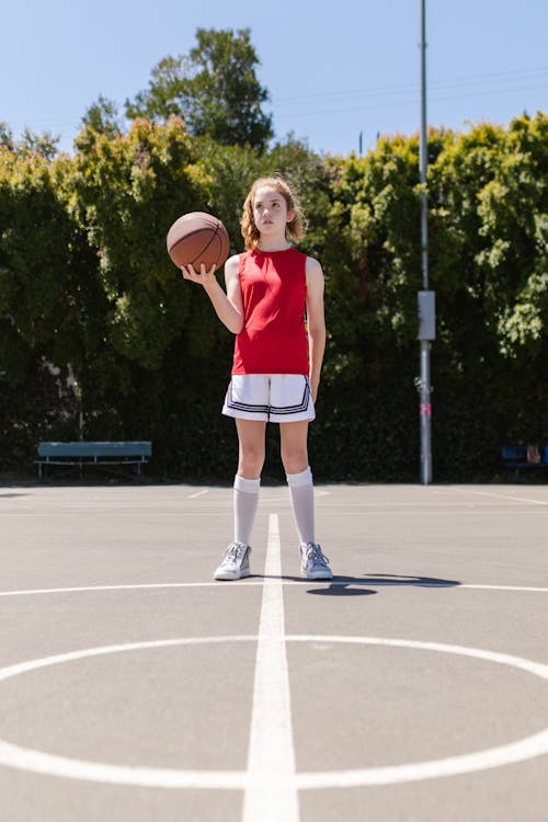 Woman in Red Shirt and White Shorts Holding Basketball