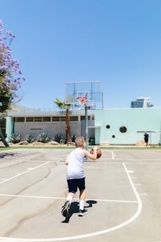 A child dribbles a basketball on an outdoor court under a clear blue sky.
