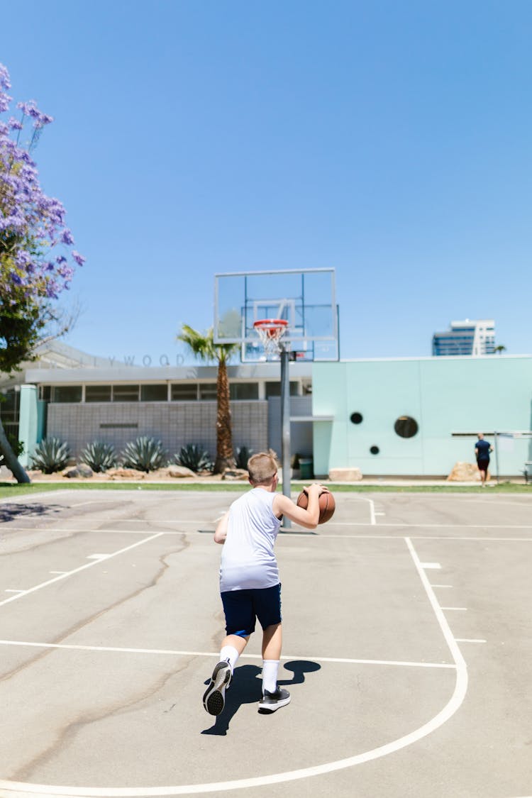 Boy In White T-shirt And Black Shorts Dribbling A Basketball