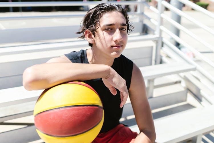 Young Man Sitting On A Bench Holding Basketball