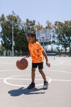 Child practicing basketball skills on an outdoor court in bright daylight.