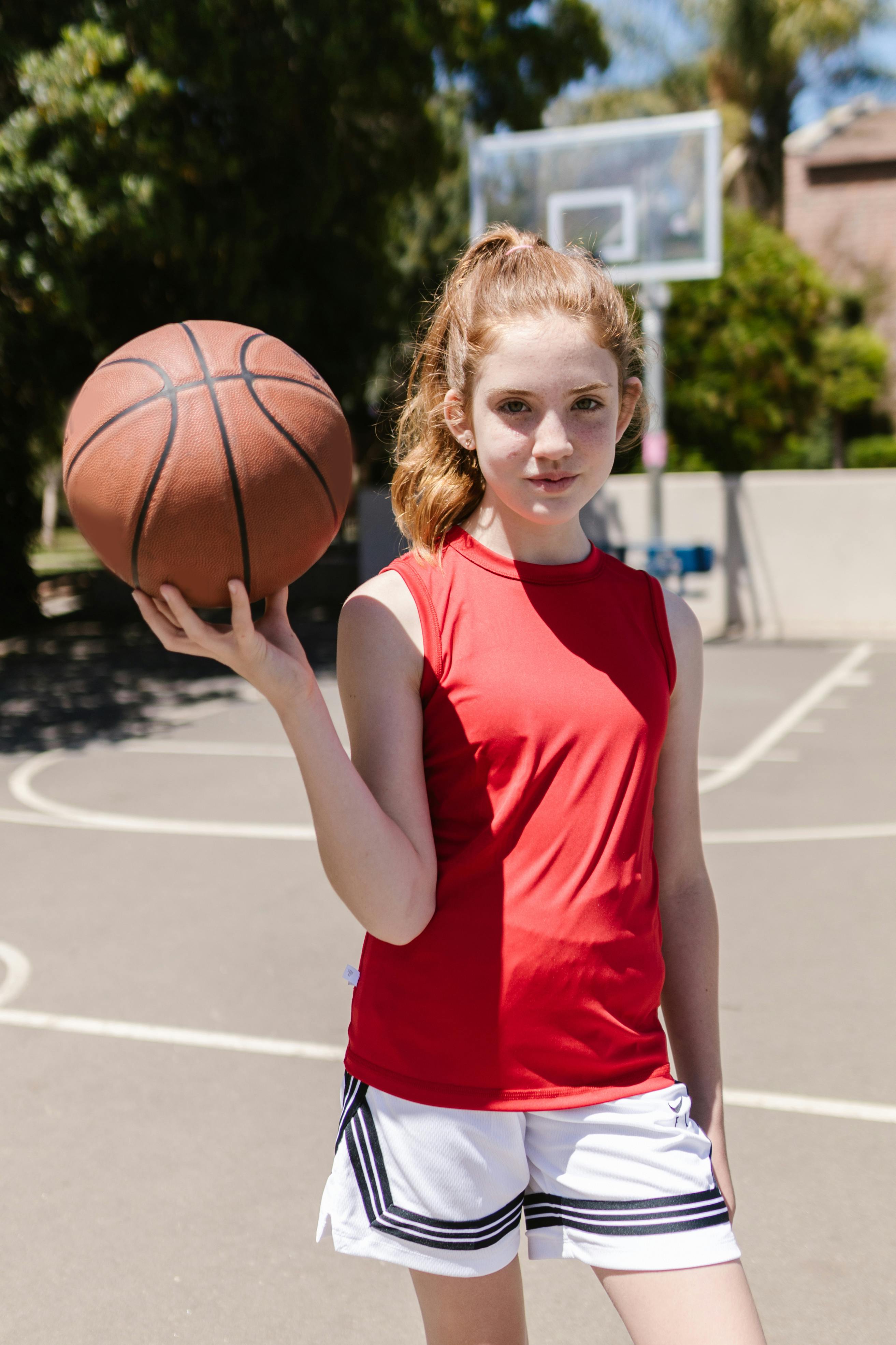 girl in red tank top with basketball on hand