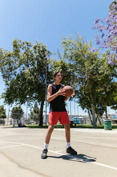 A young man playing basketball on an outdoor court surrounded by trees.