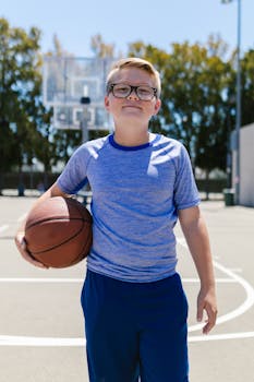 Confident young boy holding a basketball on an outdoor court on a sunny day.