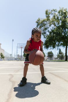 A young child dribbling a basketball on an outdoor court under clear skies, focused on play.