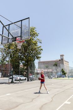 Young girl playing basketball outdoors on a sunny day.