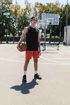 A young man holding a basketball on an outdoor court during the day, ready for a game.