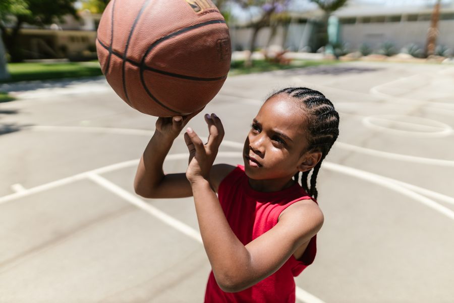 A young girl in a red jersey holding a basketball up to shoot