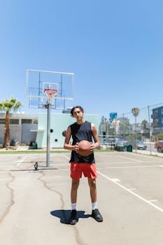 Athletic young man in activewear holding a basketball on a sunny outdoor court.