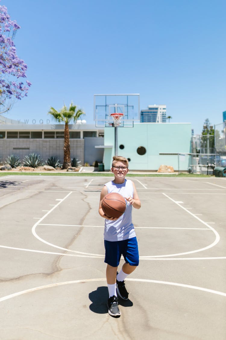 Boy In White Tank Top And Blue Shorts Holding A Basketball