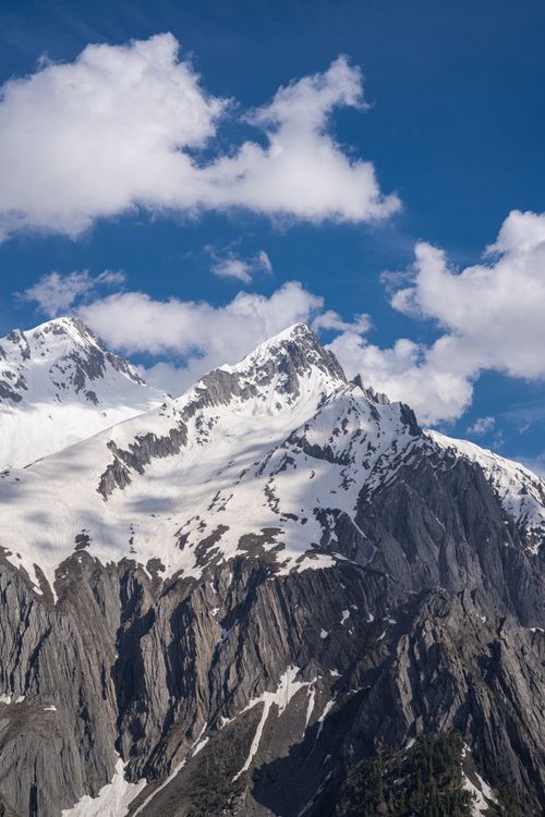 Free Majestic snow-covered mountain peaks with a vibrant blue sky and scattered clouds. Stock Photo