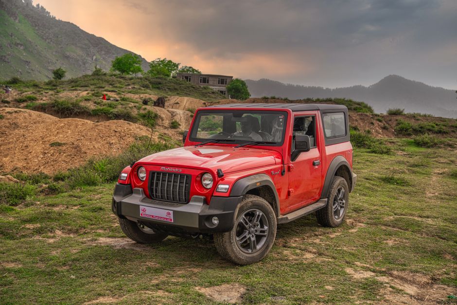 A vibrant red Mahindra Thar parked off-road in the scenic Dara mountain region of Kashmir.