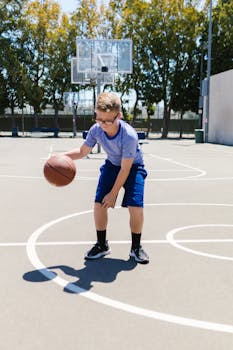 Young boy dribbling basketball on outdoor court during a sunny day.