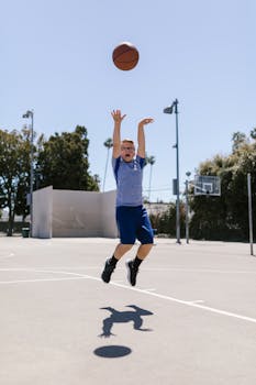 A young boy is captured mid-air while perfecting his basketball jump shot on an outdoor court.