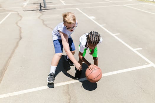 Two young boys playing basketball outdoors on a sunny day, focusing on dribbling and teamwork skills.