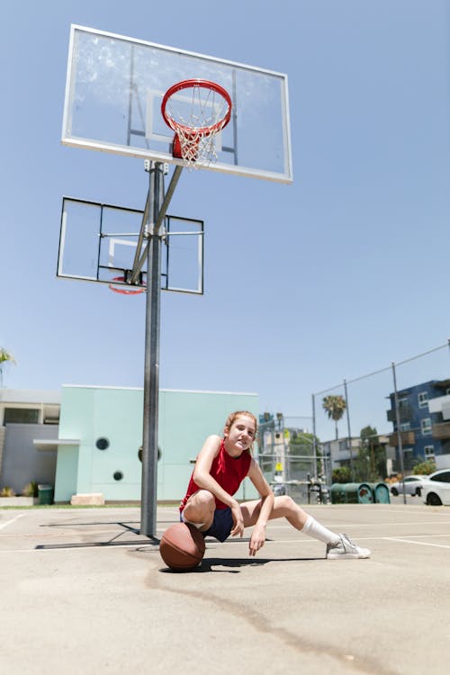 Free Young Girl Sitting Under a Basketball Hoop Stock Photo