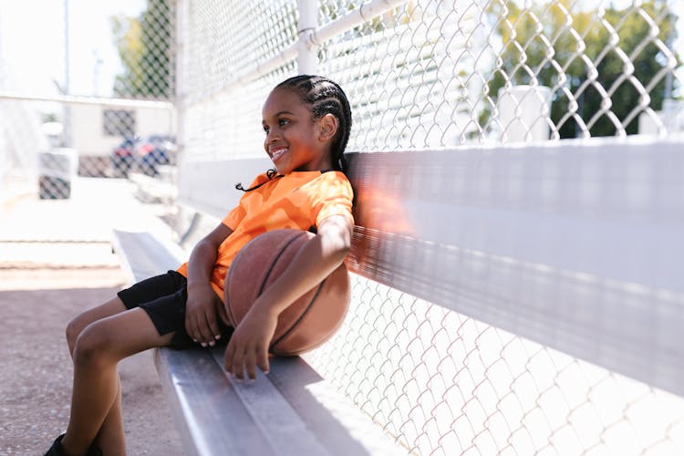 Child Holding A Ball Sitting On A Bench