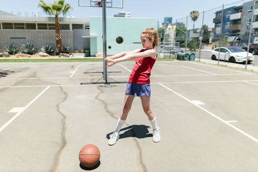 Young girl in red tank top stretching on an outdoor basketball court on a sunny day.