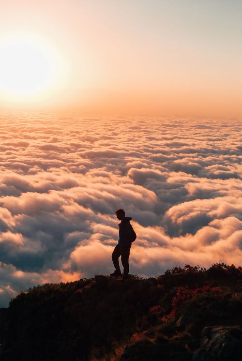 Free Person silhouetted against a stunning sea of clouds at sunset, creating a serene and ethereal scene. Stock Photo