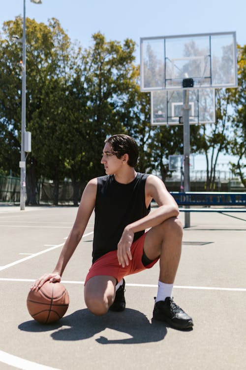 Teenager in Black Tank Top Crouching on Basketball Court