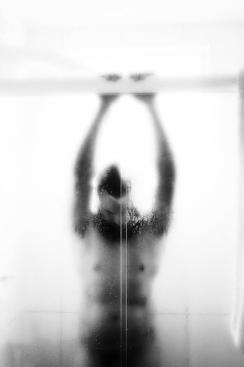 Grayscale Photo of a Person Inside a Shower Room