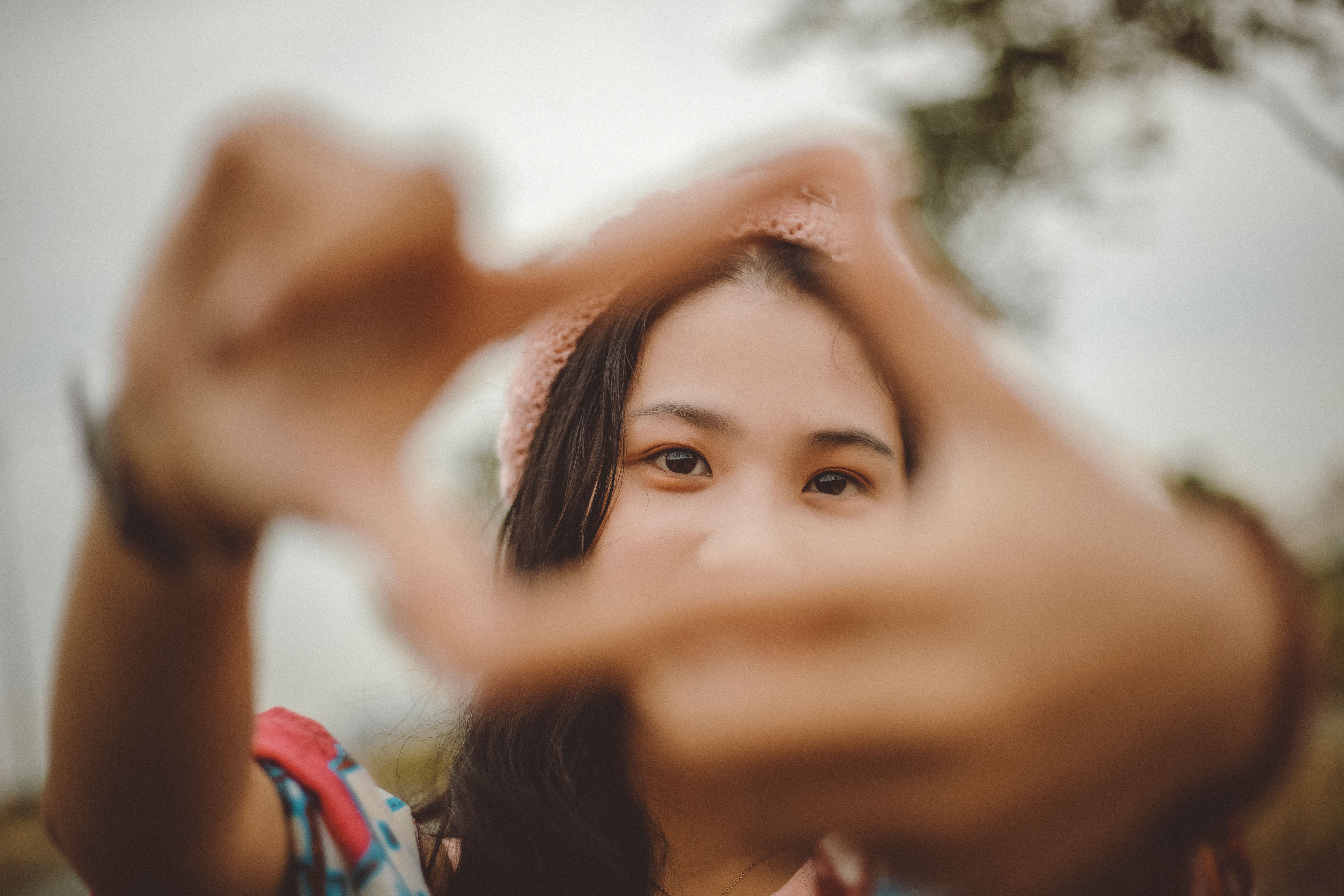 Close-up of a young woman playfully framing her face with her hands outside.