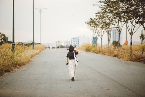 Free A woman walks down a deserted city street surrounded by nature, embodying solitude. Stock Photo