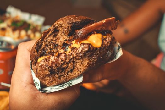 A delicious cheeseburger with bacon and melted cheese held in hand, showcasing rich, savory flavors.