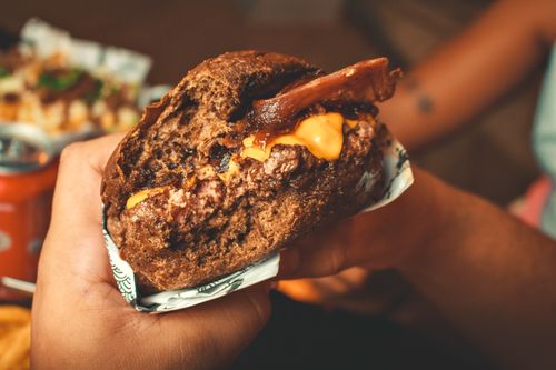 Free A delicious cheeseburger with bacon and melted cheese held in hand, showcasing rich, savory flavors. Stock Photo